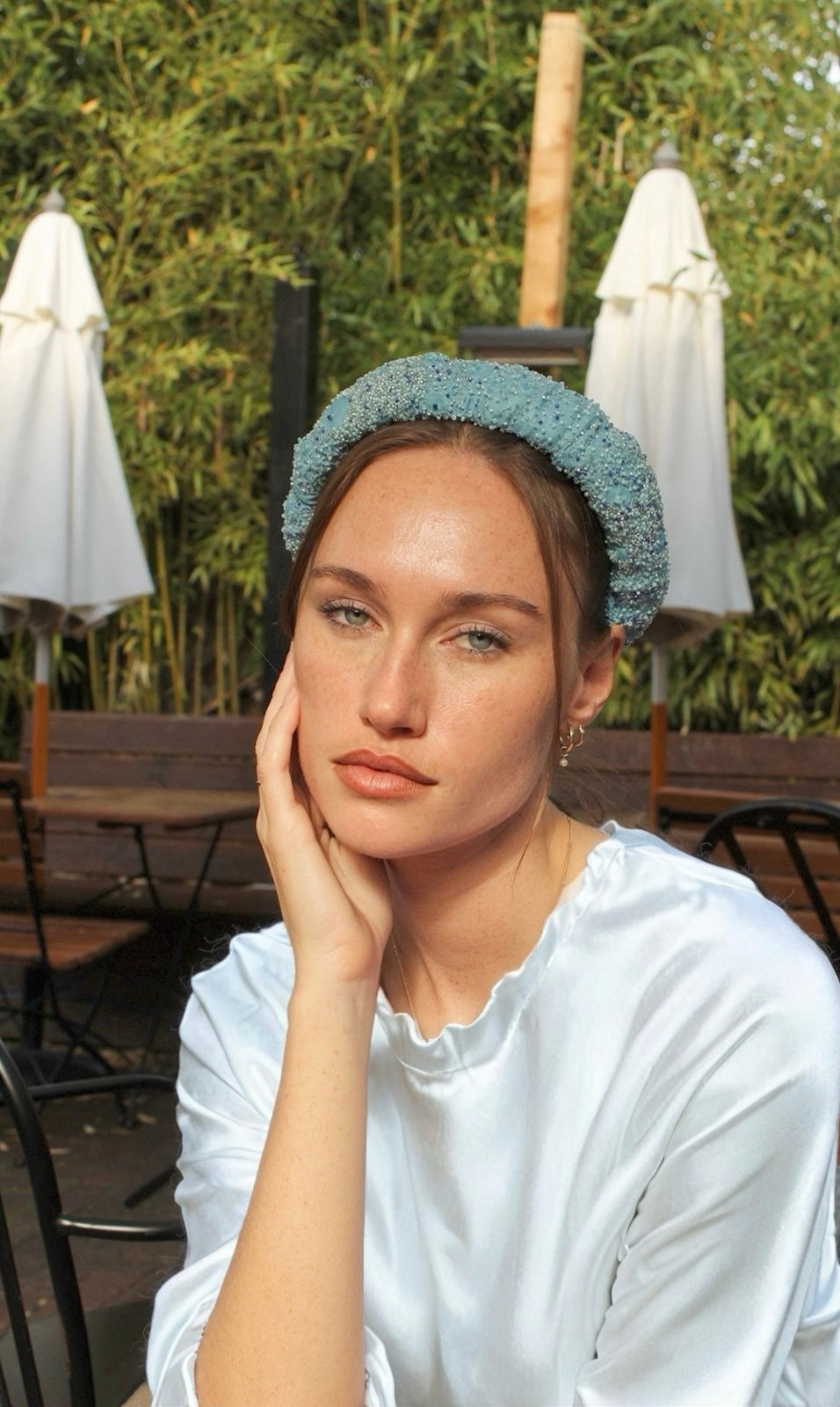 Woman wearing a light blue bridal headband in an outdoor setting with tables and umbrellas.