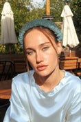 Load image into Gallery viewer, Woman wearing a light blue bridal headband in an outdoor setting with tables and umbrellas.

