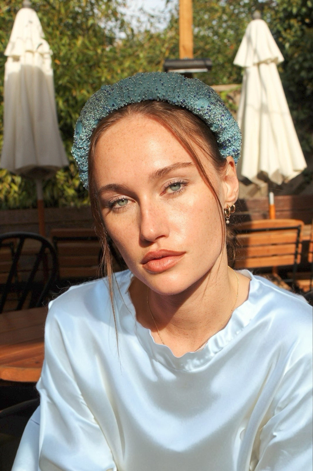 Woman wearing a light blue bridal headband in an outdoor setting with tables and umbrellas.