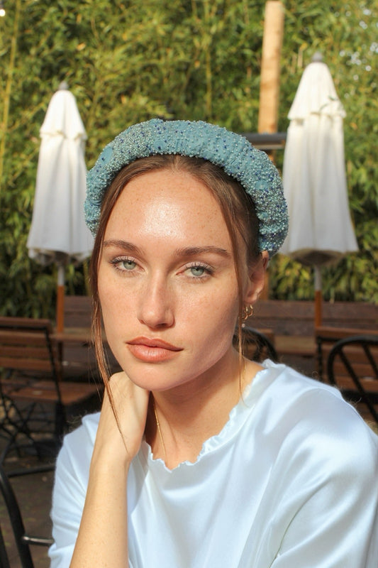 Woman wearing a light blue bridal headband in an outdoor setting with tables and umbrellas.