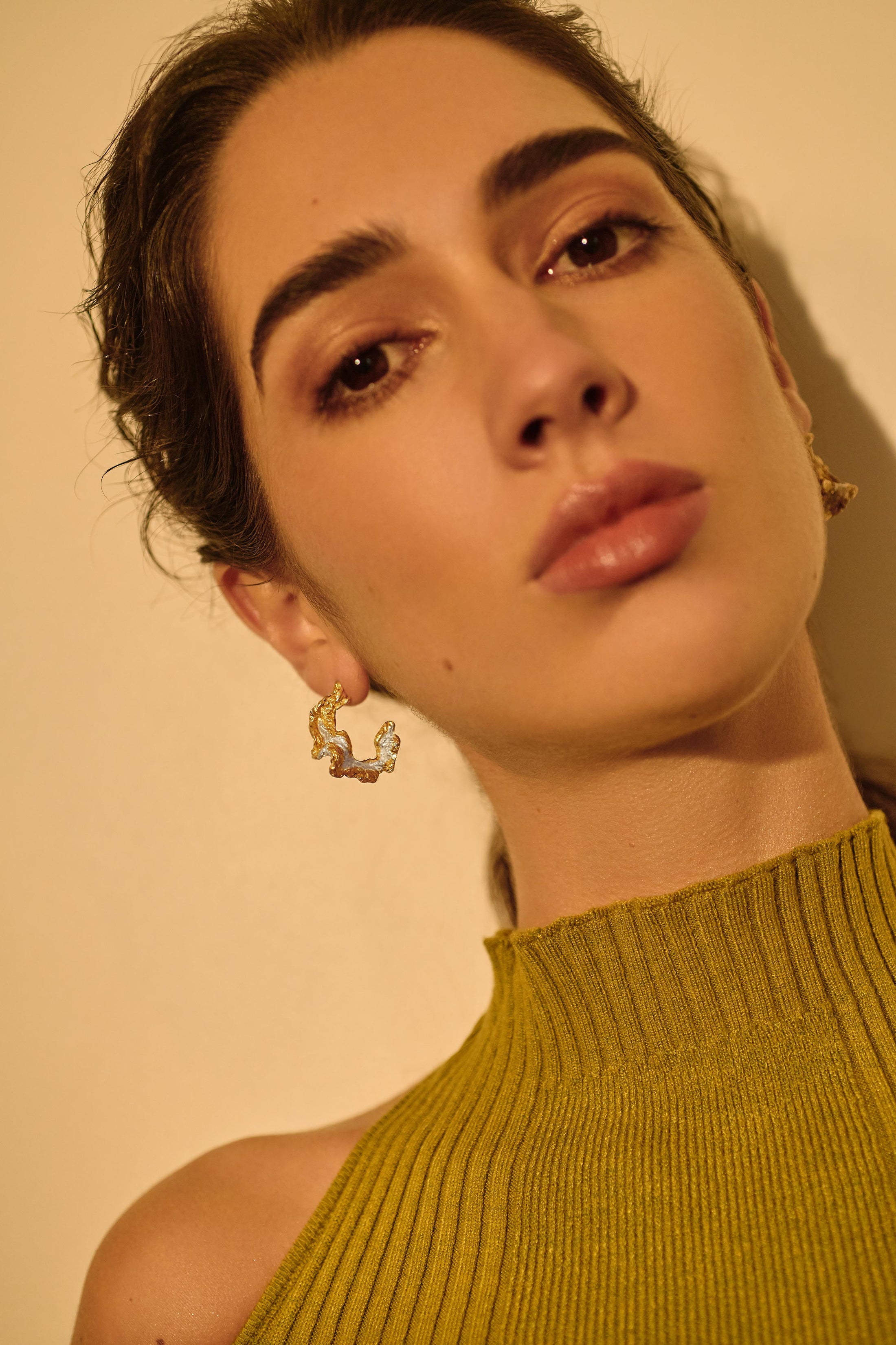 Woman wearing gold earrings against a beige background