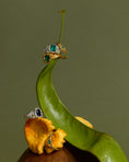 Load image into Gallery viewer, Gold and silver ring with emerald stones on a green leaf with yellow flowers.
