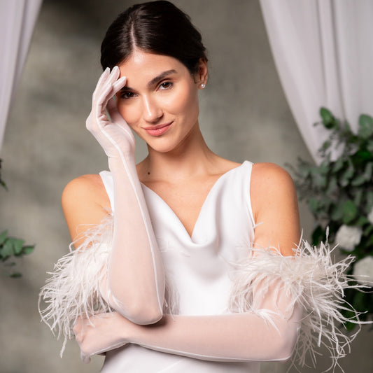 Woman wearing a white dress with feathered sleeves and white gloves against a neutral background
