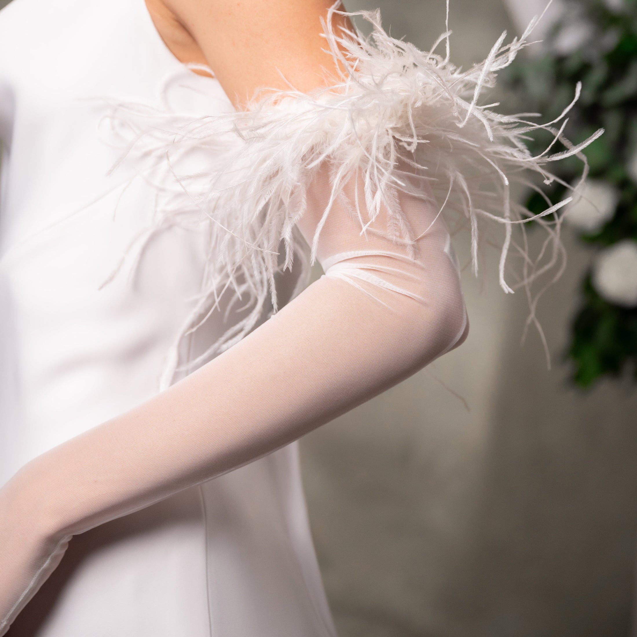White feathered arm cover worn by a person, with a blurred background.