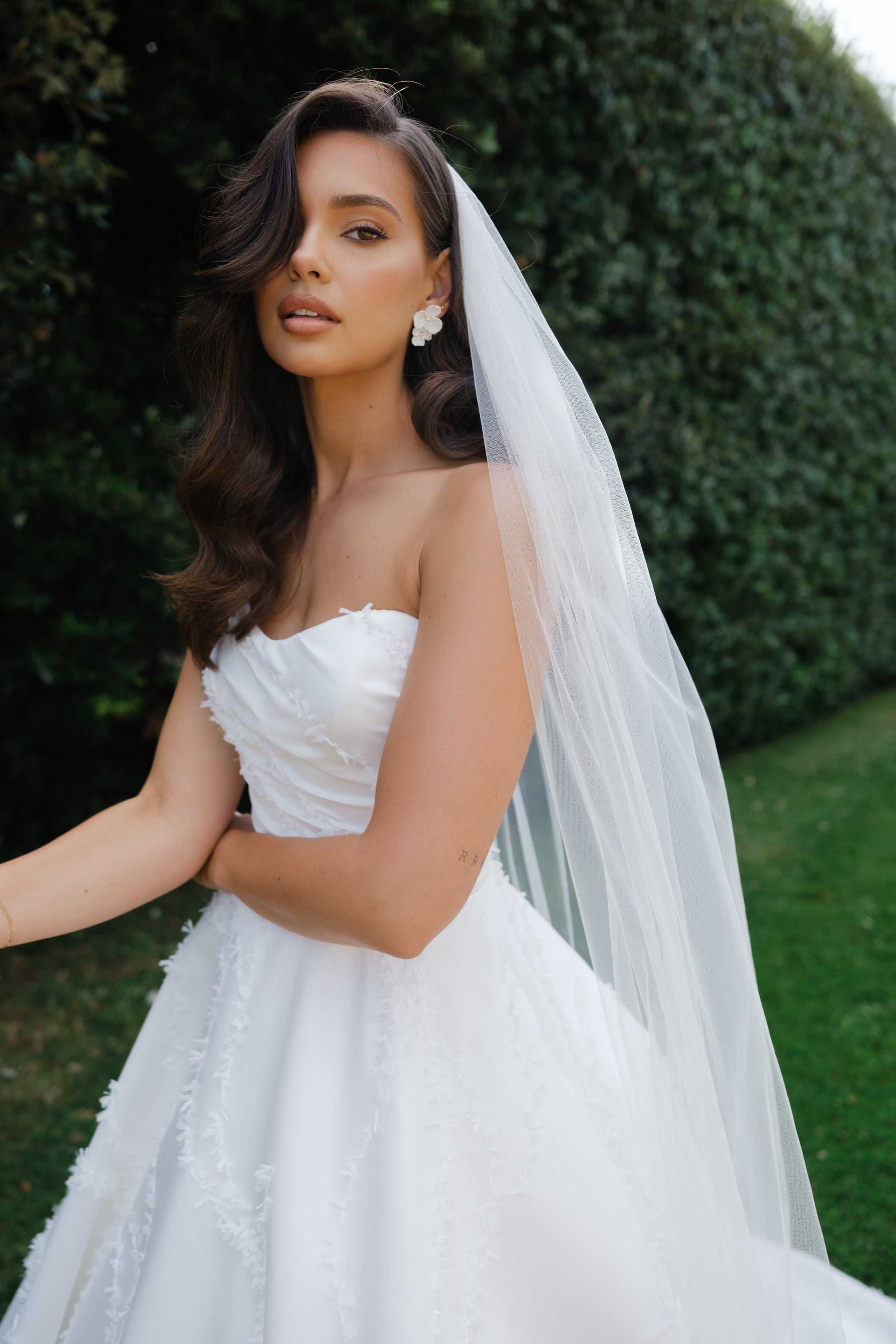 Woman in a white wedding dress with a veil standing outdoors.