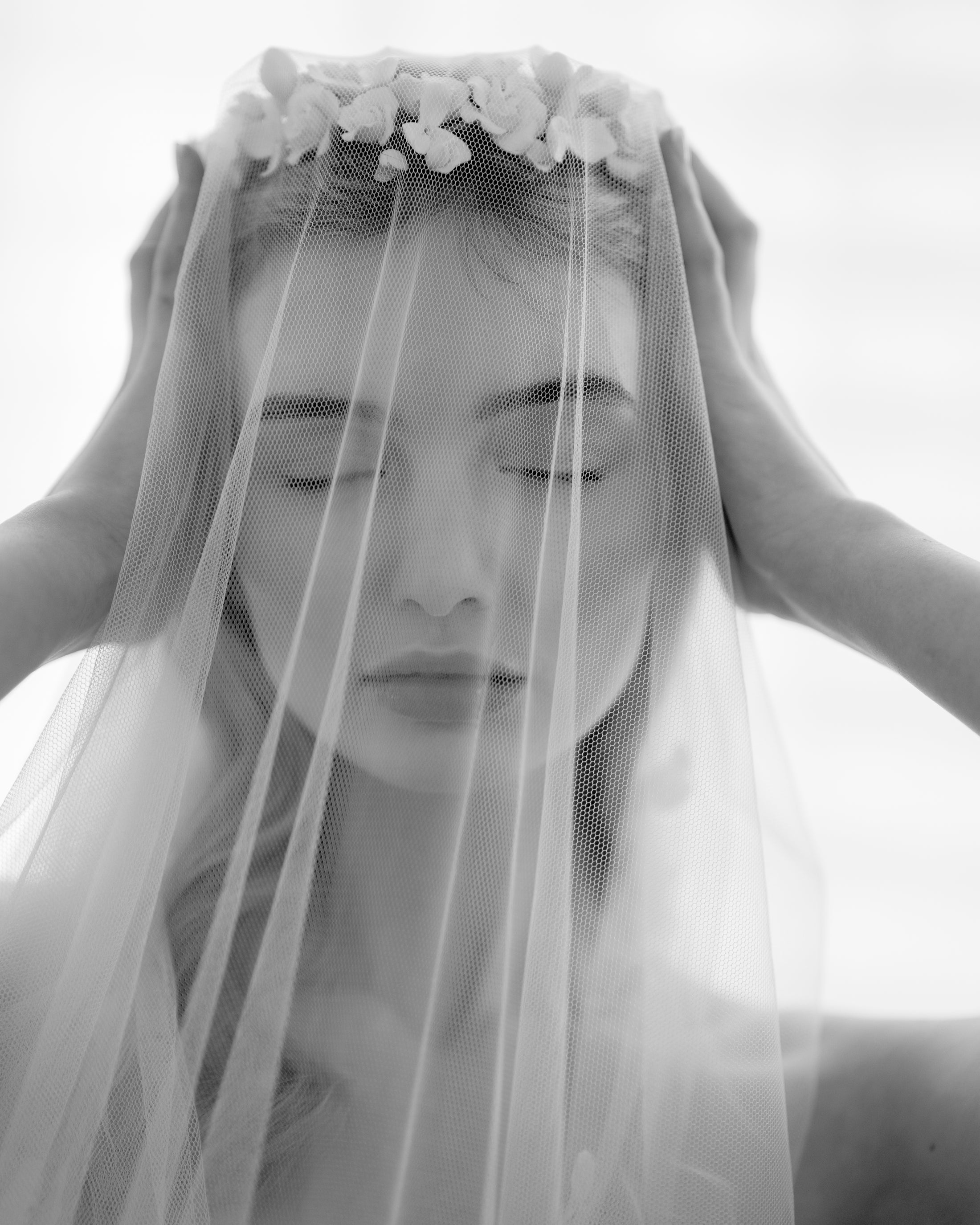 Black and white photo of a person wearing a veil with floral accents.