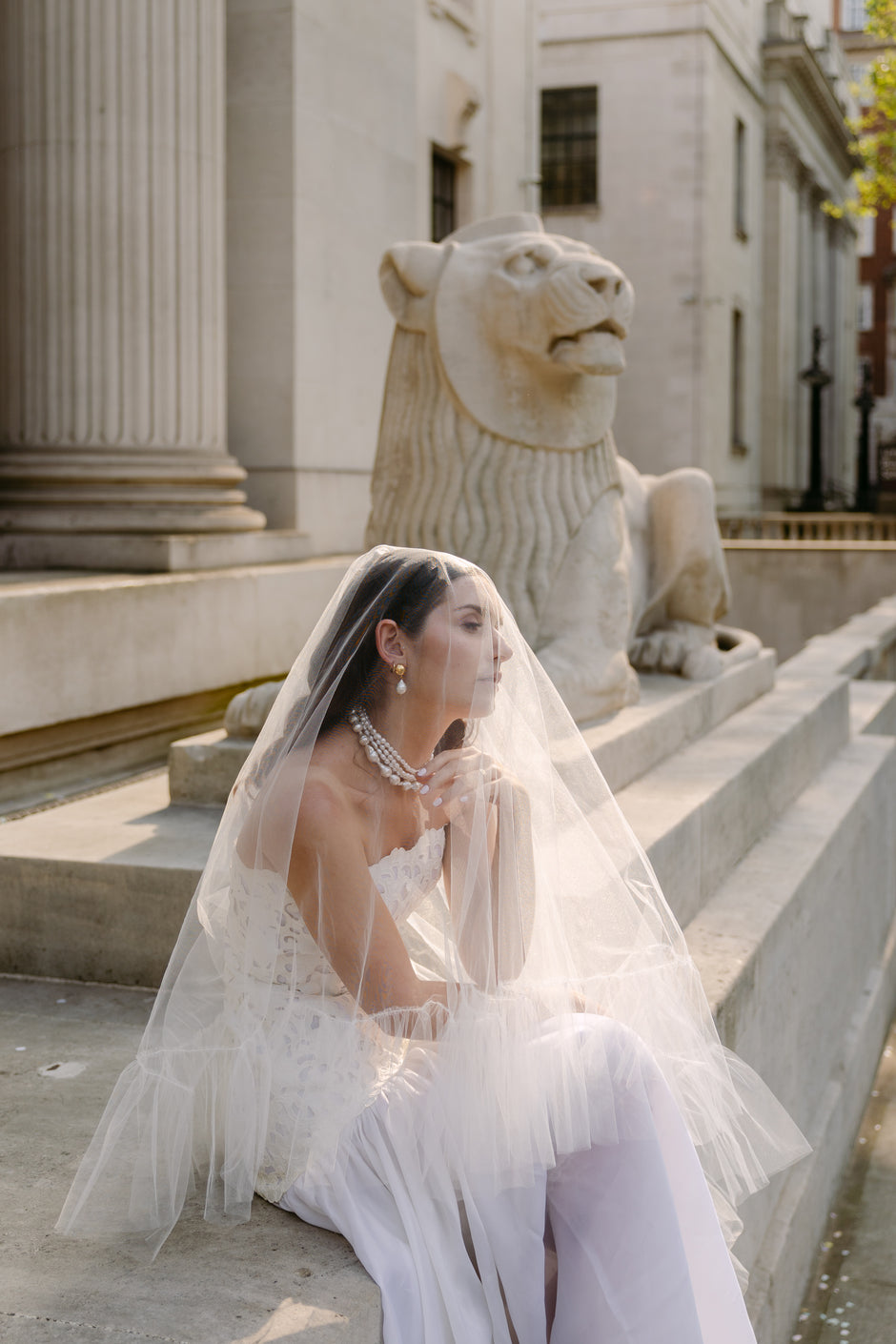 Woman in a wedding dress sitting on steps with a lion statue in the background