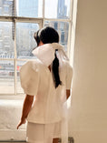 Load image into Gallery viewer, Person wearing a white outfit with a bridal bow standing in front of a window with cityscape view.
