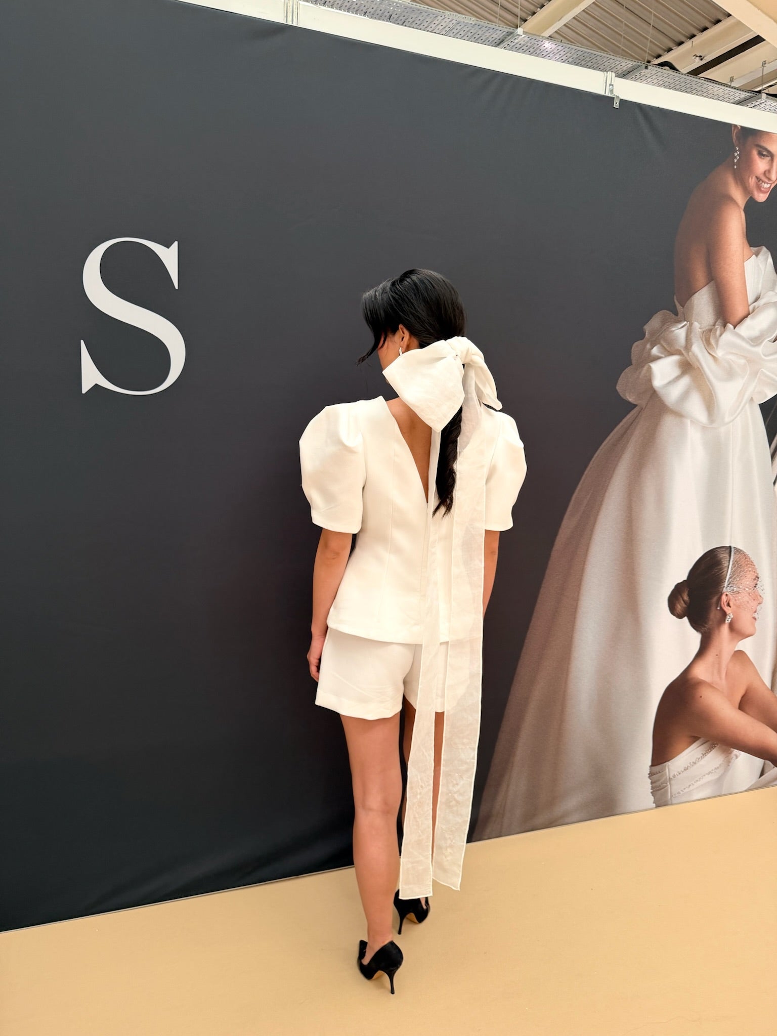Woman in a white outfit standing in front of a branded backdrop with a large 'S' logo.