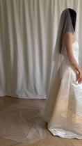 Load image into Gallery viewer, Bride wearing a white wedding dress with a plain veil against a white curtain background.
