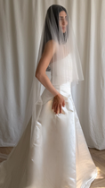 Load image into Gallery viewer, Bride wearing a white wedding dress with a plain veil against a white curtain background.
