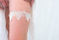 Load image into Gallery viewer, A white lace garter belt with pearl accents worn on a person's thigh, framed by white fabric.
