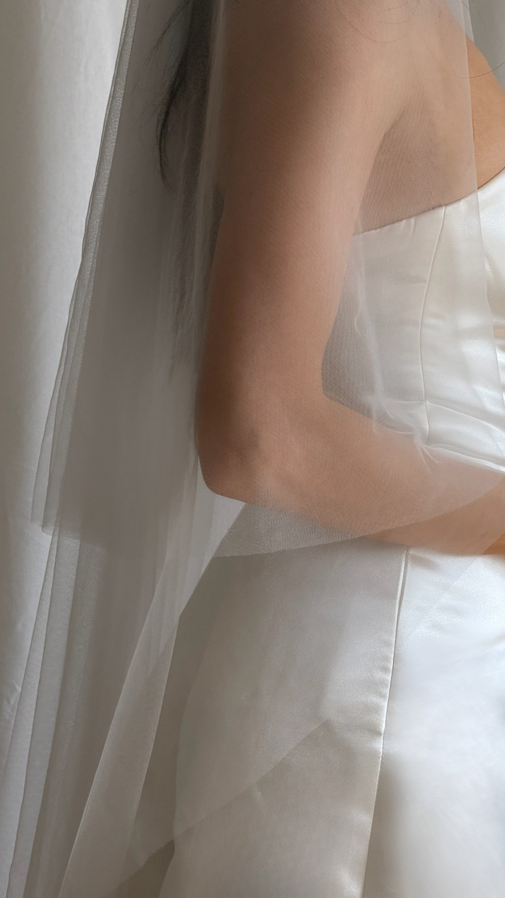 Bride wearing a white wedding dress with a plain veil against a white curtain background.