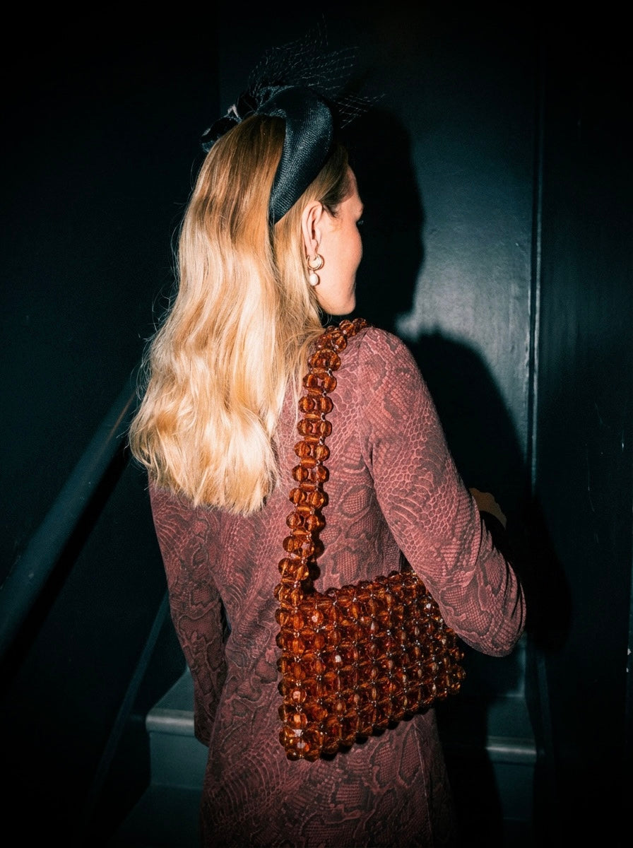 Woman holding a brown beaded bridal handbag against a dark background