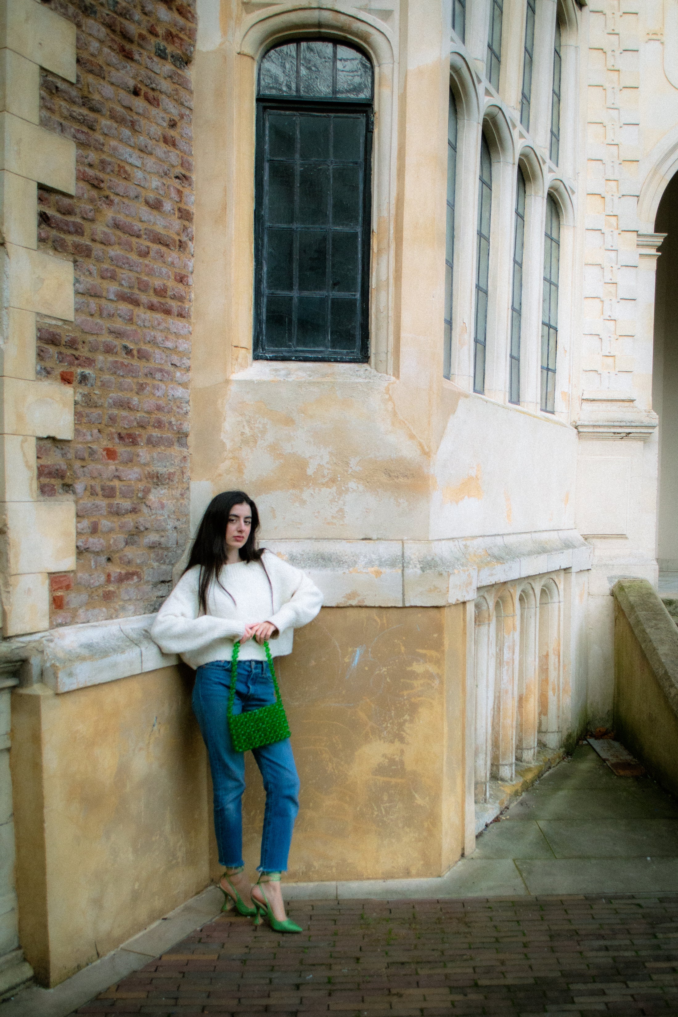 Woman standing against a stone wall of a building holding a green beaded bridal handbag