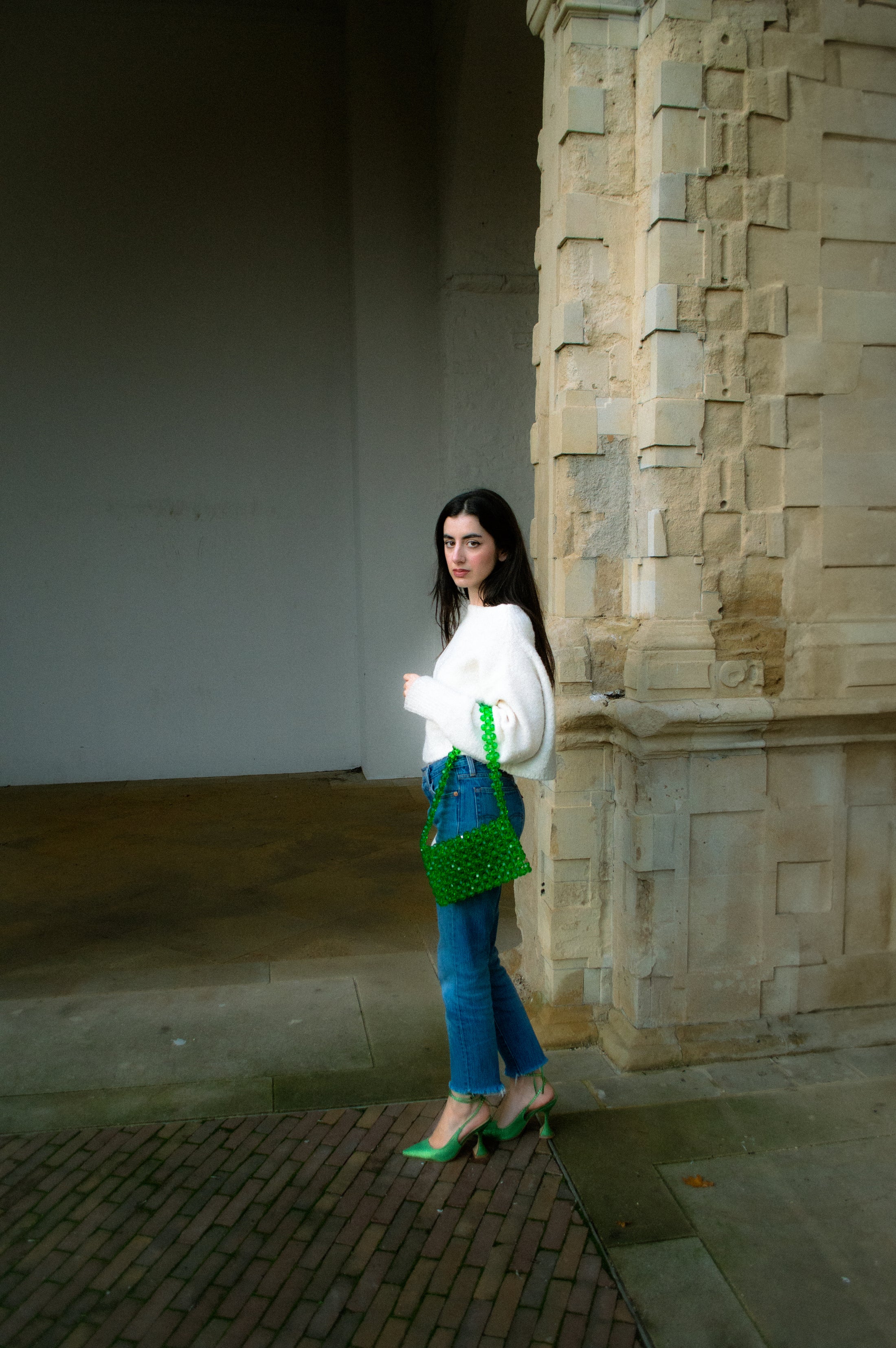 Woman standing against a stone wall holding a green bridal handbag handbag