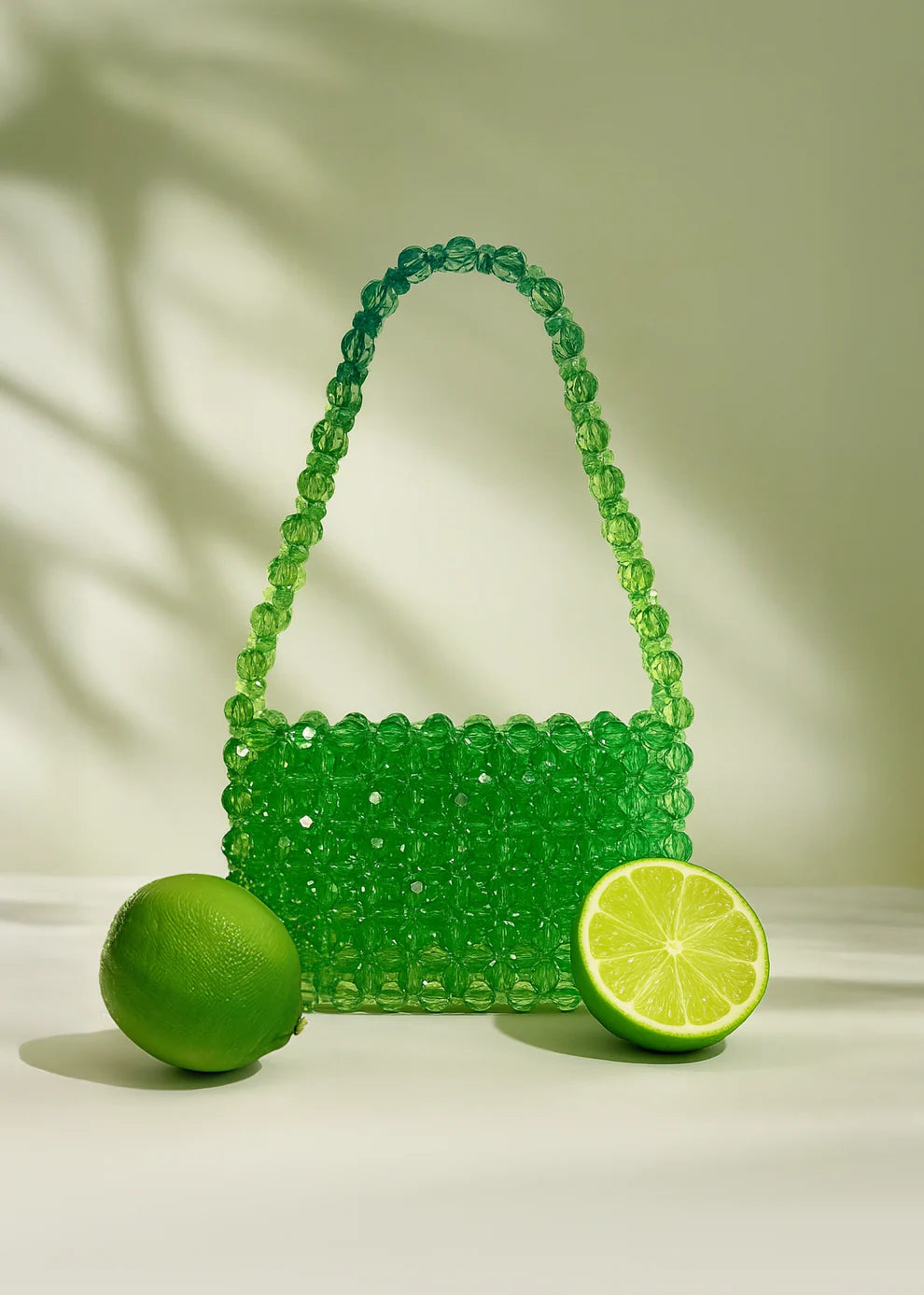 Green beaded bridal handbag with two limes on a light background