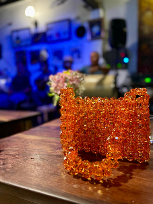 Orange beaded bridal bag on a wooden surface with a blurred indoor background