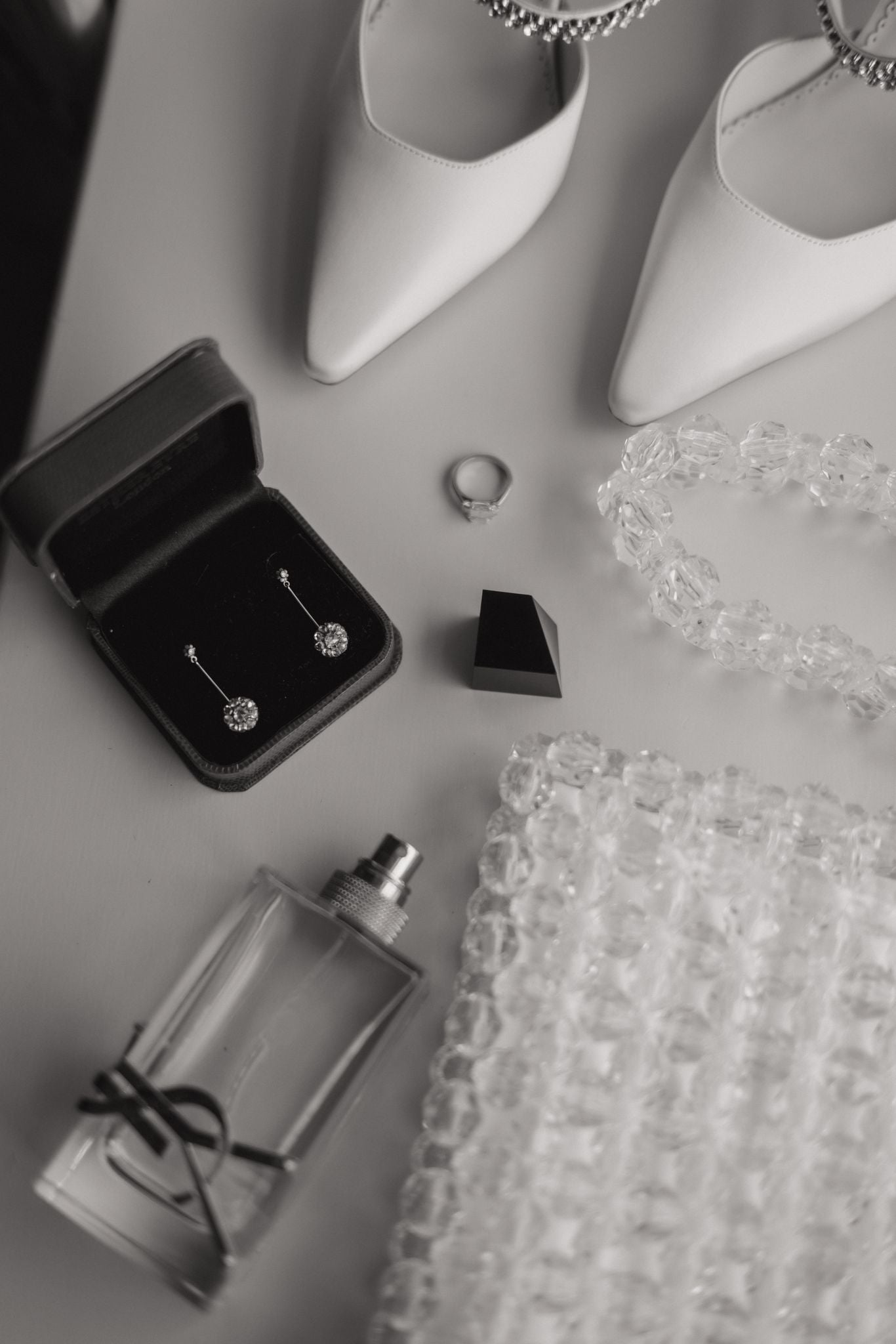 Jewelry including earrings, a ring, a bridal bag, and a small bottle on a textured surface.