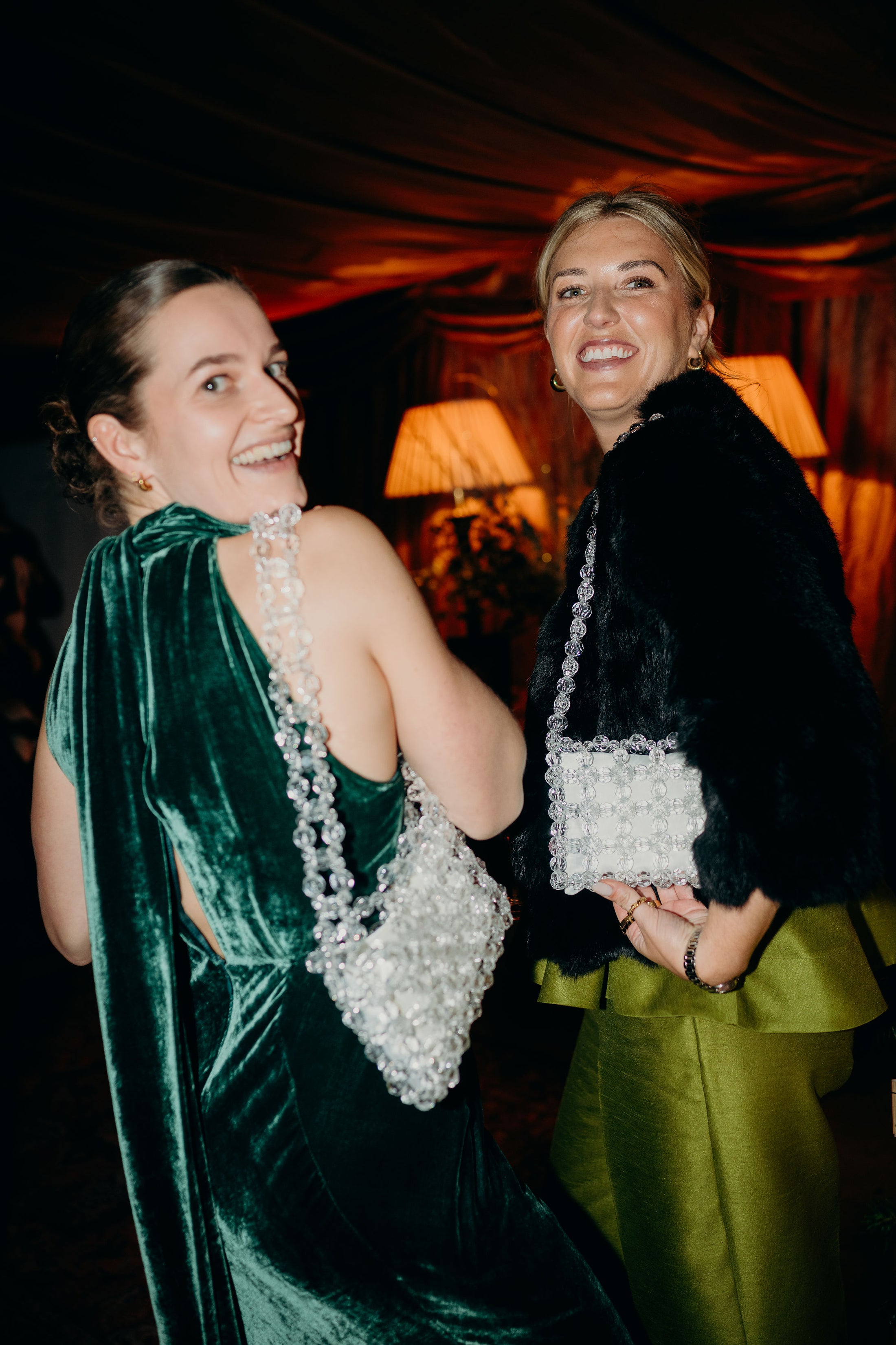 Two women in formal attire with decorative accessories, standing close together wearing a bridal bag