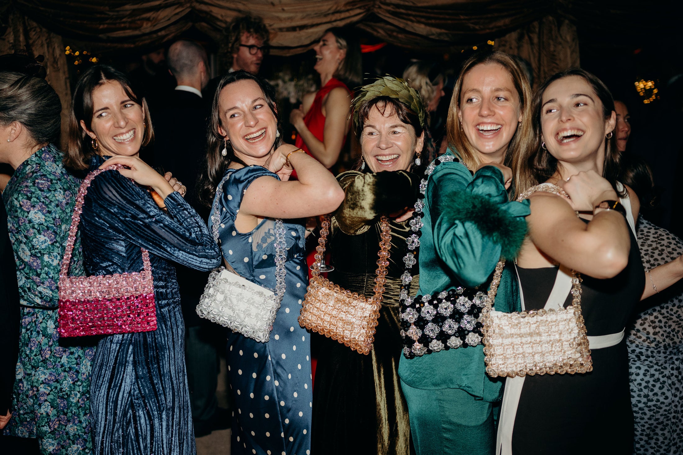 Group of women posing together at a social event, holding bridal bags.