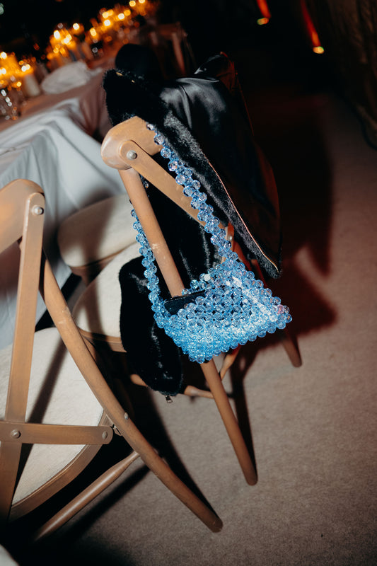 Blue beaded bridal bag on a chair with a blurred background of a room with tables and lights.