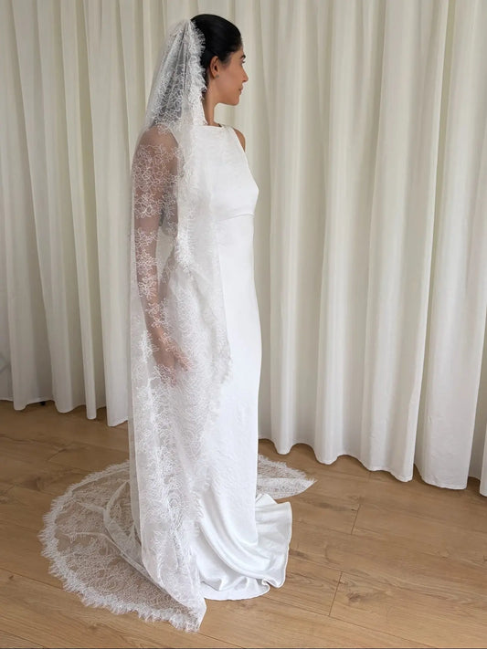 Woman wearing a white lace veil and wedding dress against a white curtain background