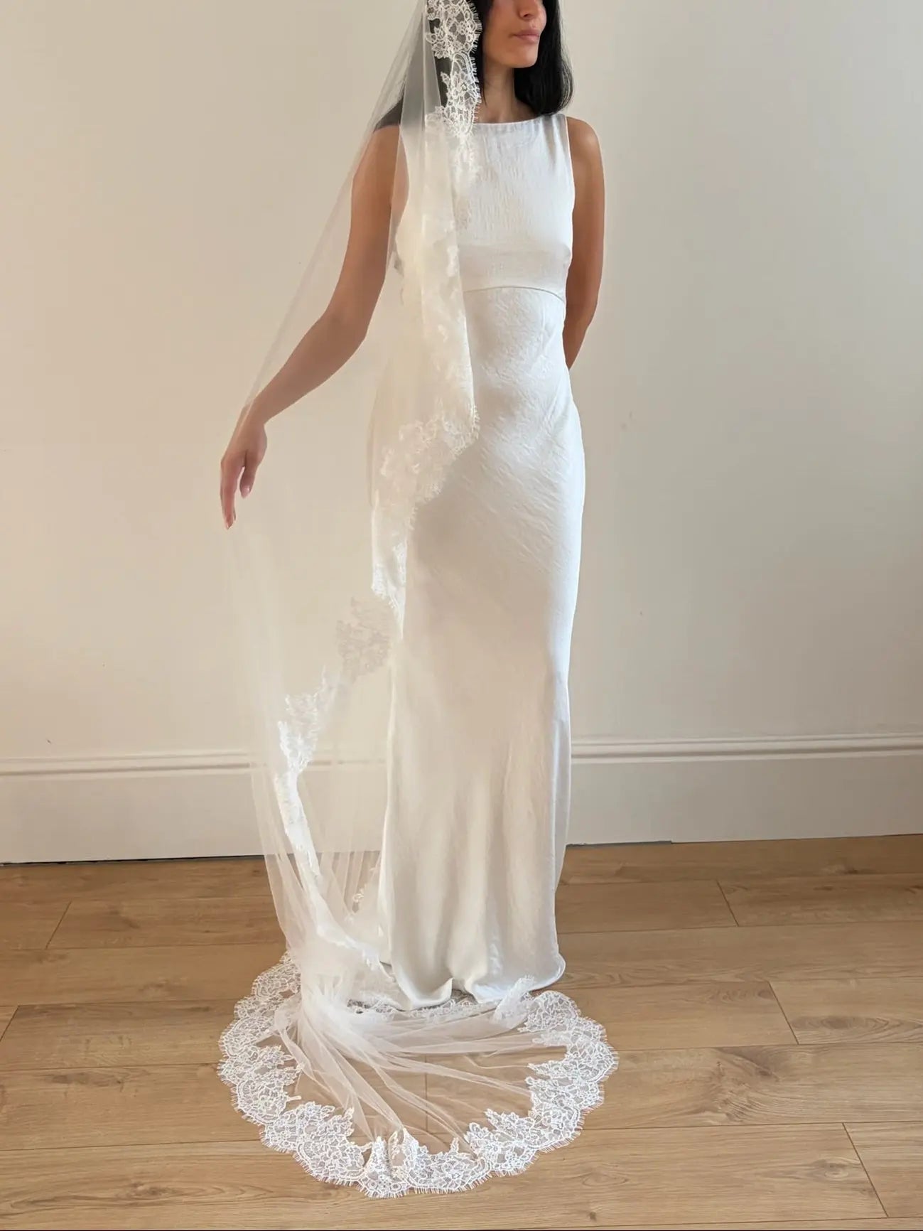 Model wearing White lace veil and wedding dress on a wooden floor with a plain white wall background