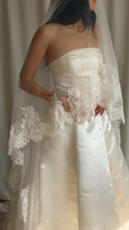 Load image into Gallery viewer, Bride wearing a white wedding dress with a lace veil against a white curtain background.
