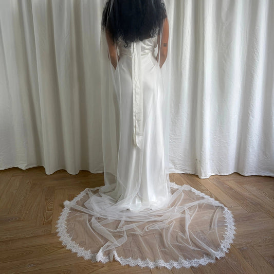Person wearing a white wedding dress with a wedding veil in front of white curtains.