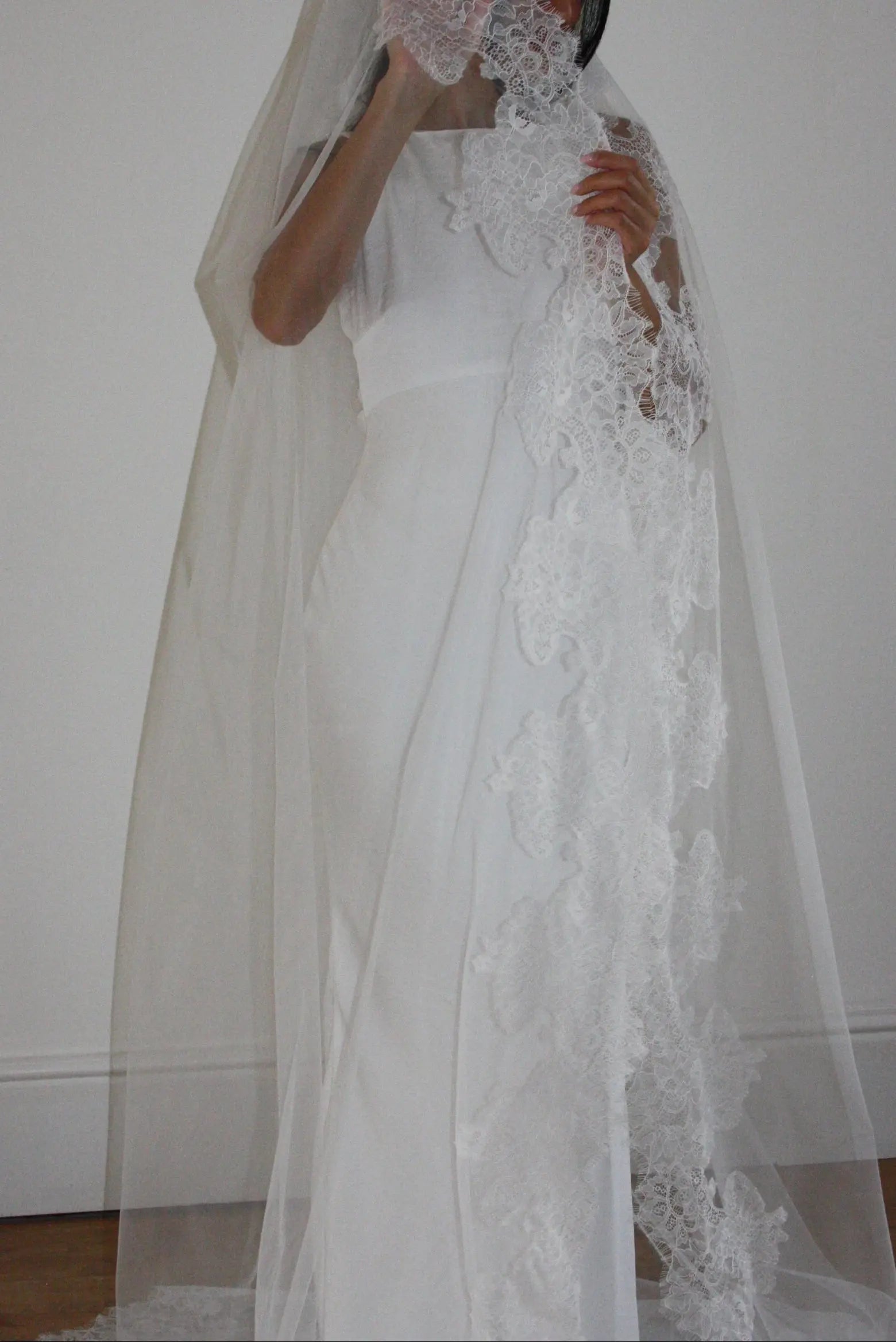 White lace veil and wedding dress on a wooden floor with a plain white wall background
