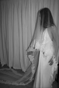 Load image into Gallery viewer, Black and white photo of a person in a wedding dress with a long lace trim veil against a curtain backdrop.

