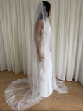 Load image into Gallery viewer, White lace veil and wedding dress on a wooden floor with a plain white wall background
