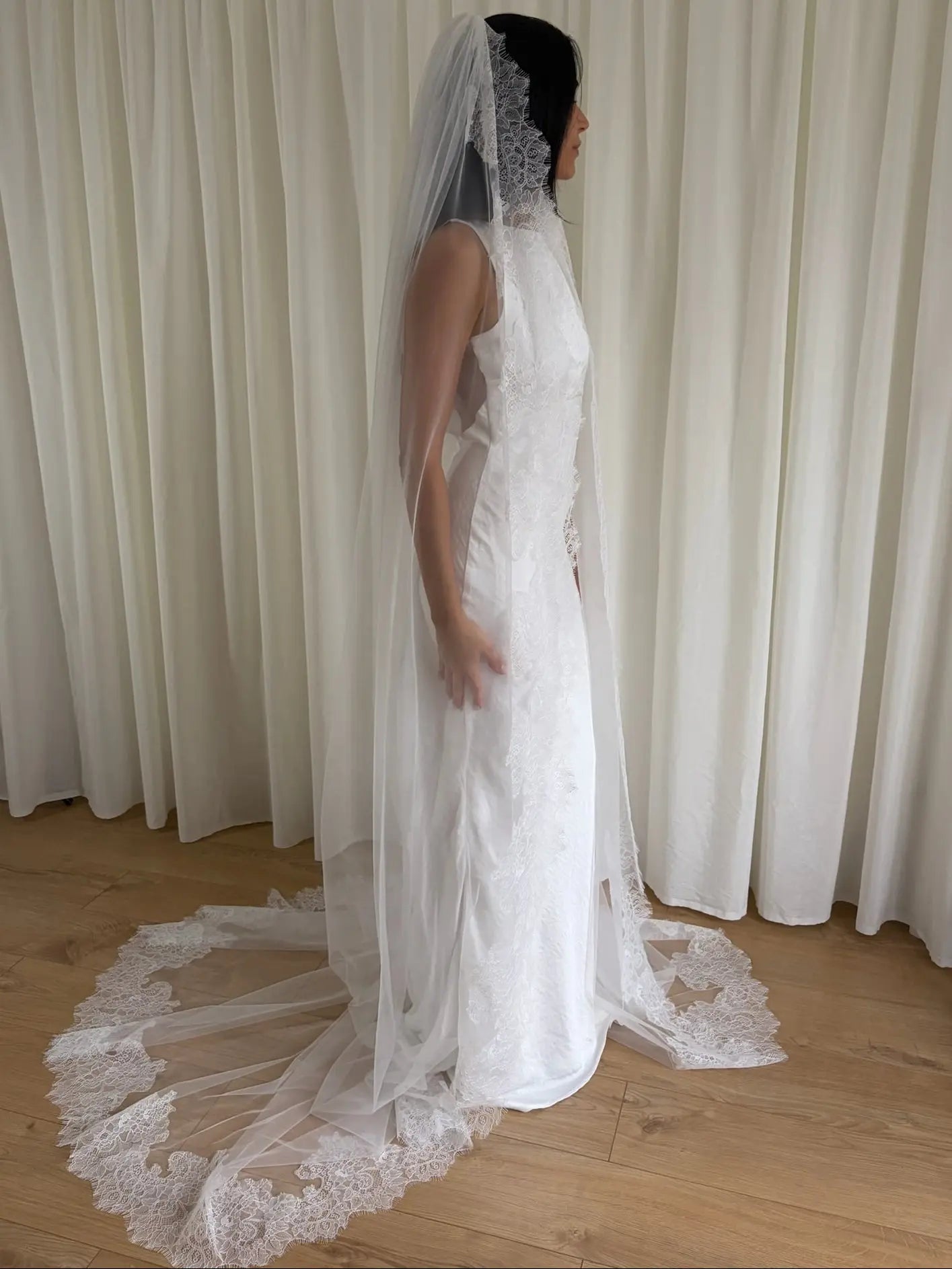 White lace veil and wedding dress on a wooden floor with a plain white wall background