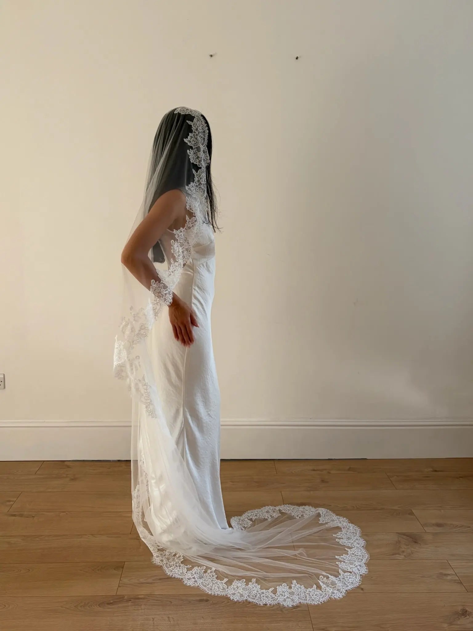 Model wearing White lace veil and wedding dress on a wooden floor with a plain white wall background