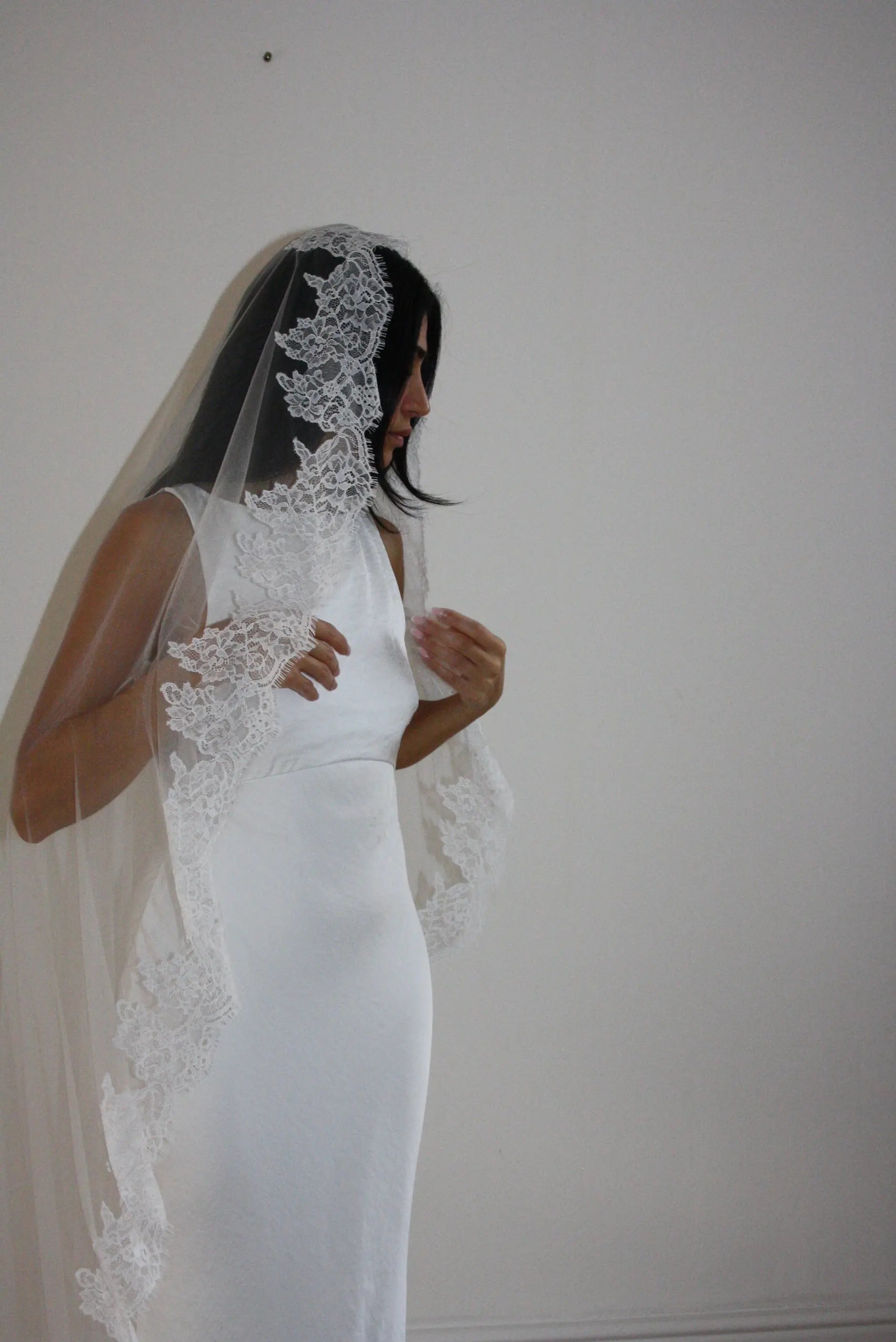 Model wearing White lace veil and wedding dress on a wooden floor with a plain white wall background