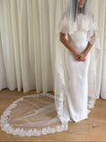 Load image into Gallery viewer, White wedding dress with a long lace veil in front of a white curtain.
