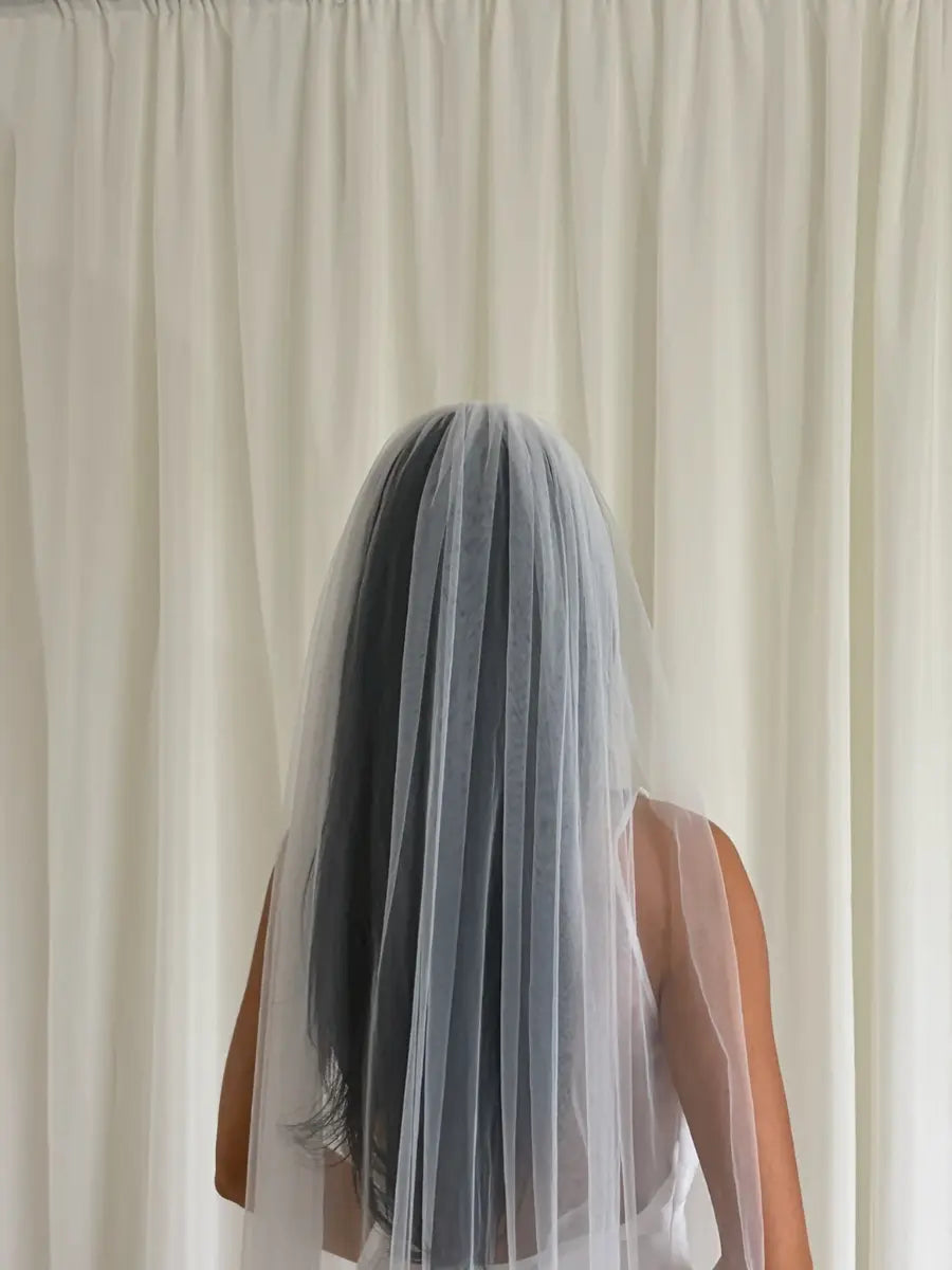 Person wearing a white wedding dress with a long plain veil against a plain background
