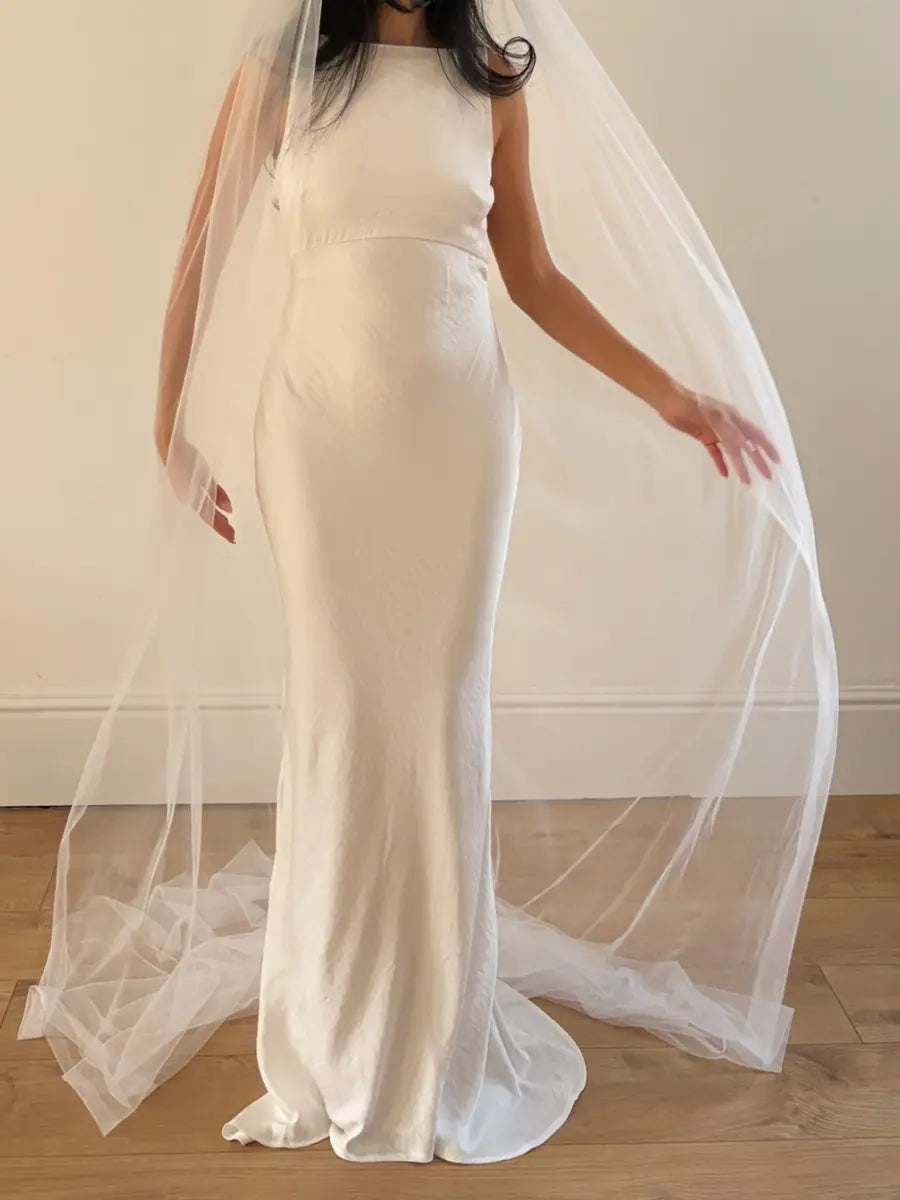 Person wearing a white wedding dress with a long plain veil against a plain background