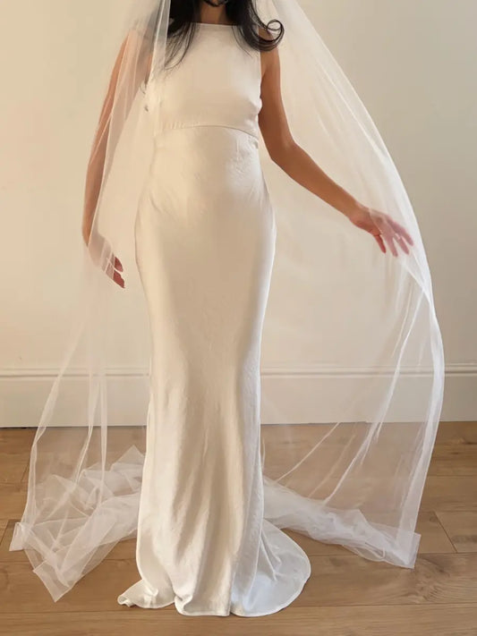 Person wearing a white wedding dress with a long plain veil against a plain background