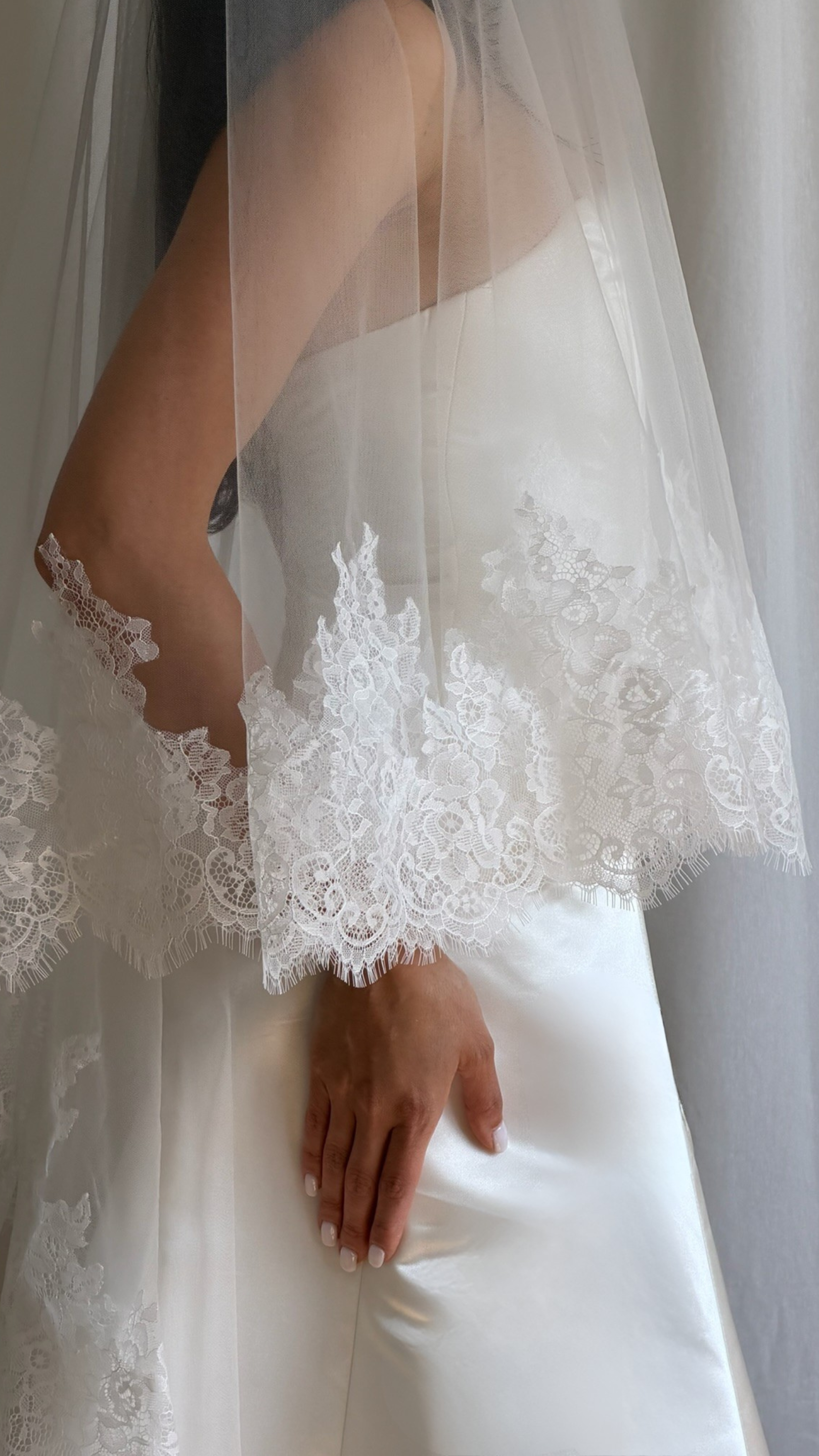 close up of bride wearing a white wedding dress with a lace veil against a white curtain background.