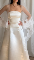 Load image into Gallery viewer, Bride wearing a white wedding dress with a lace veil against a white curtain background.
