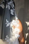 Load image into Gallery viewer, A close-up of a bridal veil with intricate white floral lace embroidery, worn by a model in warm, direct sunlight.
