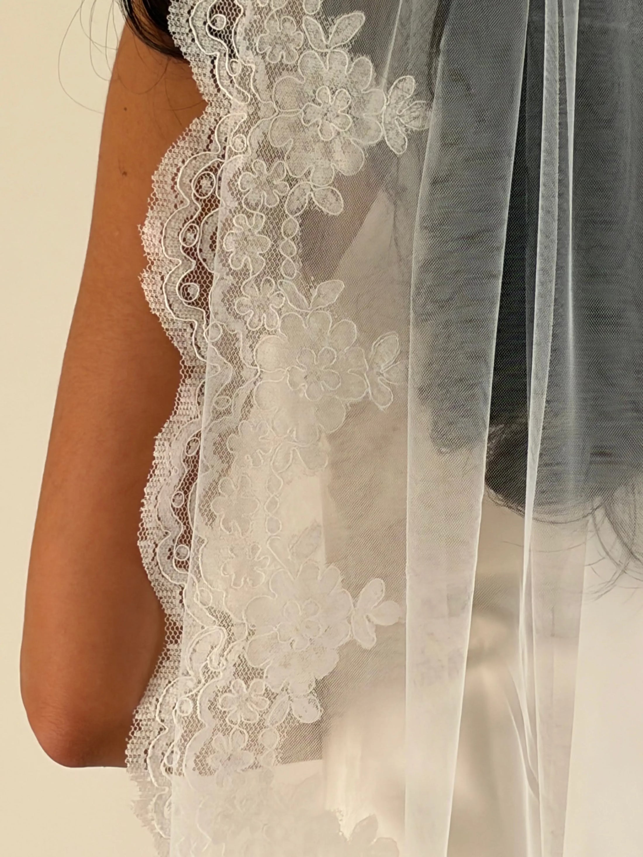 White floral lace bridal veil with a long sheer tulle layer, shown draped over a model's shoulder.