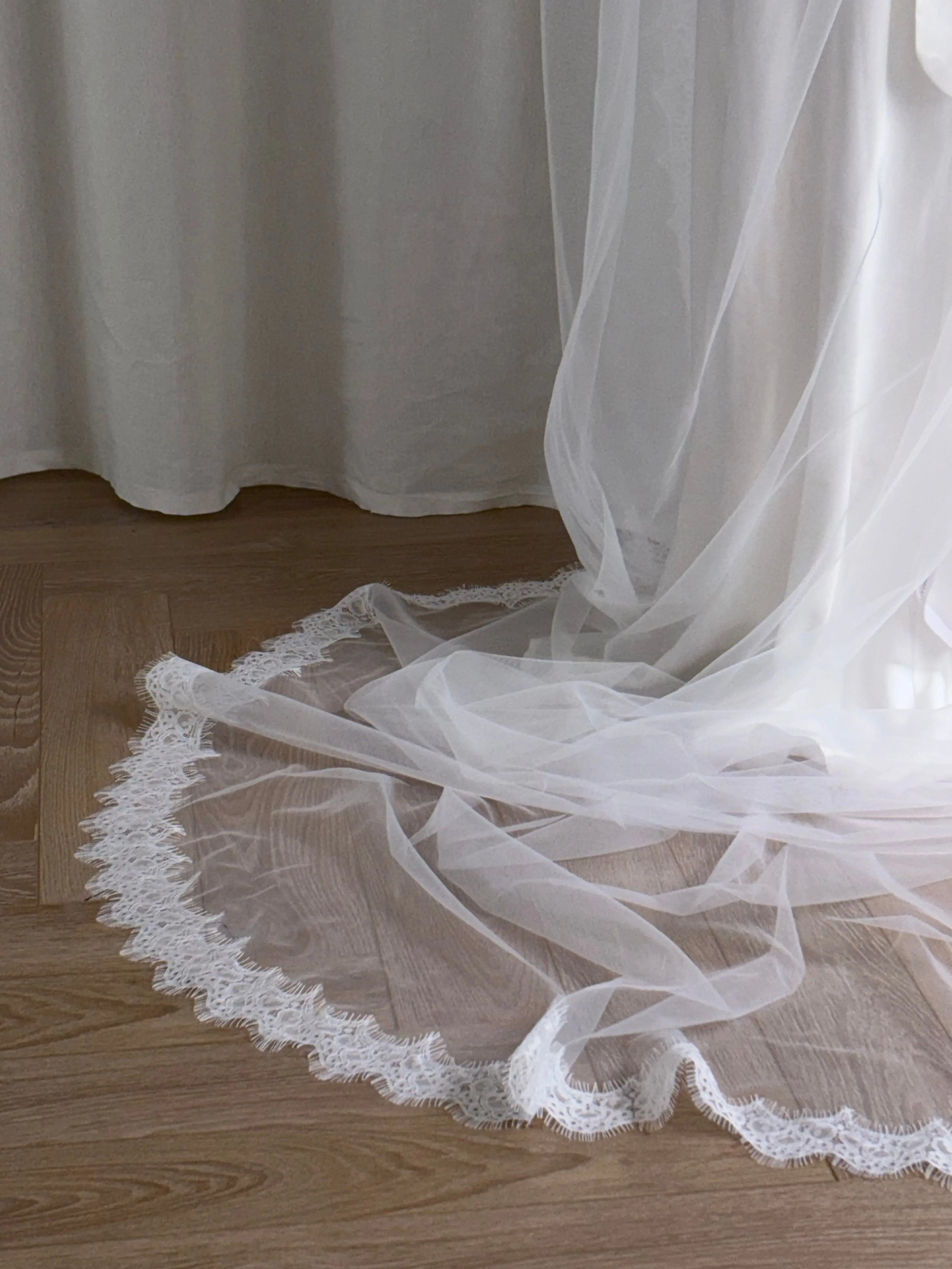 Lace trim wedding veil in front of a white curtain on a wooden floor