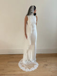 Load image into Gallery viewer, Woman wearing a white wedding dress with a long lace veil on a plain background
