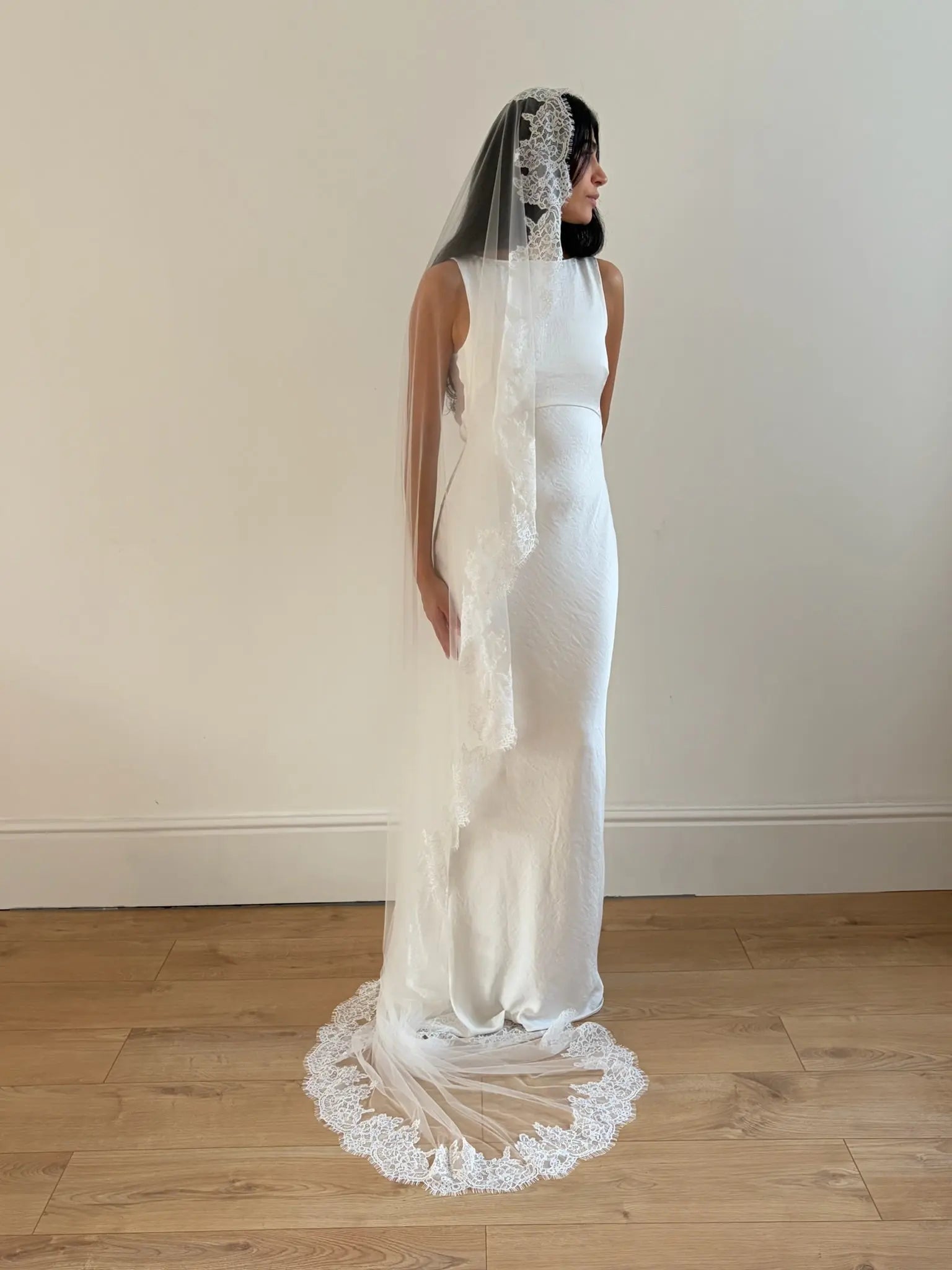 Woman wearing a white wedding dress with a long lace veil on a plain background