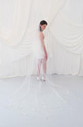 Load image into Gallery viewer, A woman wearing a sheer white bridal veil with delicate bow details and a short white slip dress, standing in front of draped white fabric.
