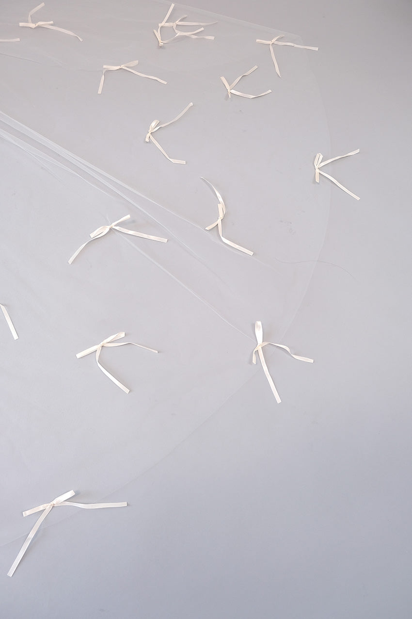 A sheer white tulle veil with multiple small white ribbon bows scattered across a light gray background.