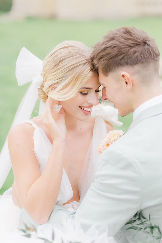 Married couple in formal attire sitting close together with a blurred green background with bride wearing silk flower bridal earrings